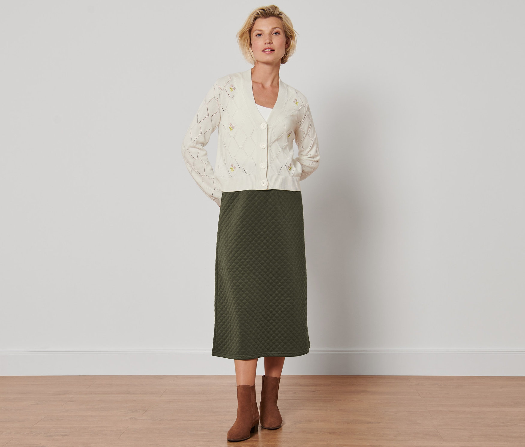 Femme posant en jupe verte aspect matelassé et cardigan.