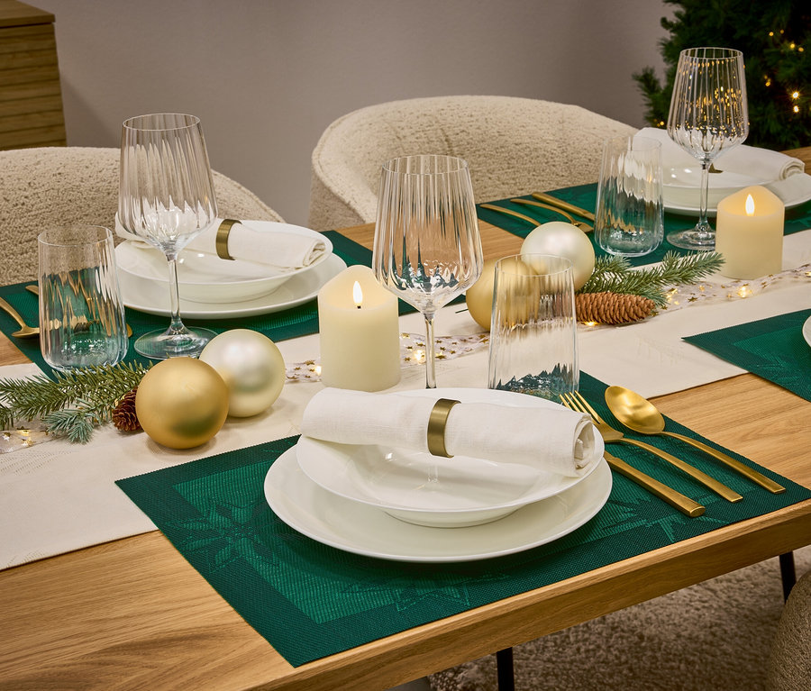 Une table dressée avec de la vaisselle blanche, des verres, des couverts dorés, des sets de table verts et des décorations de Noël.