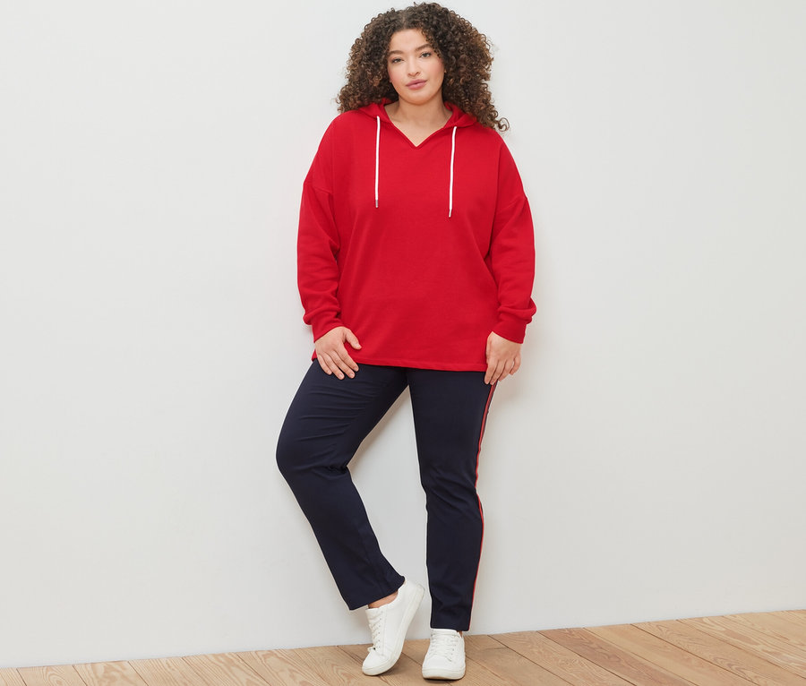 Femme posant dans un sweat à capuche rouge et un pantalon stretch avec des galons.
