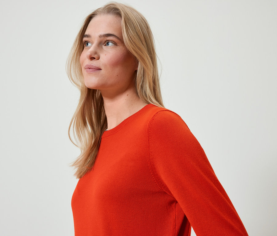 Portrait d'une femme blonde portant un pull orange, regardant vers la gauche.