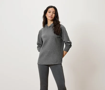 Une femme pose en pull à capuche gris et pantalon à motifs.