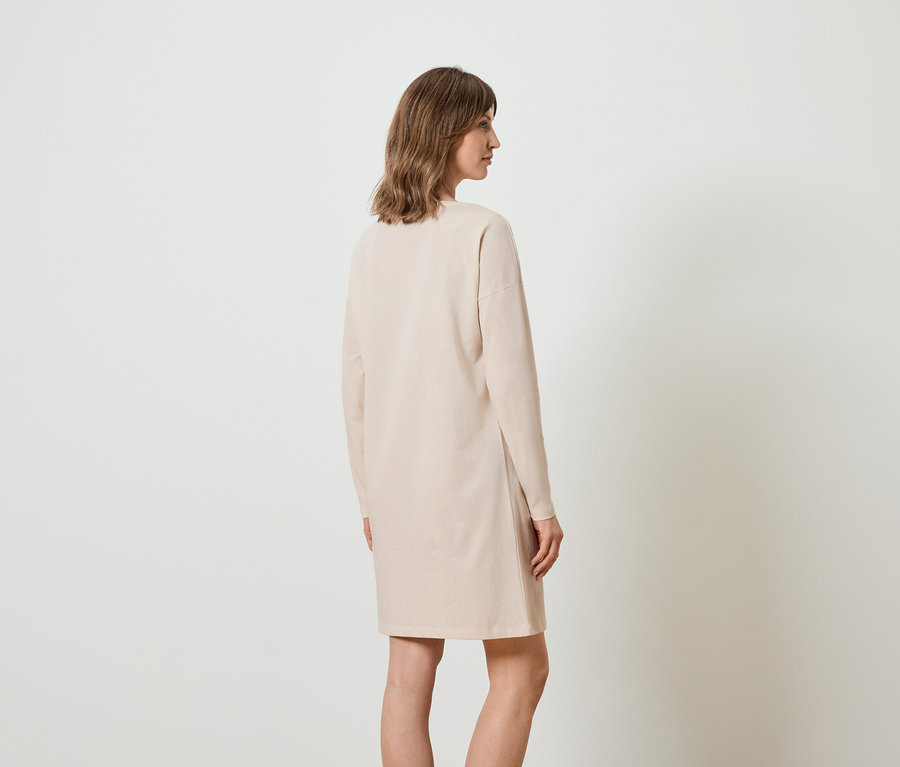 Femme portant une robe longue beige, vue de dos.