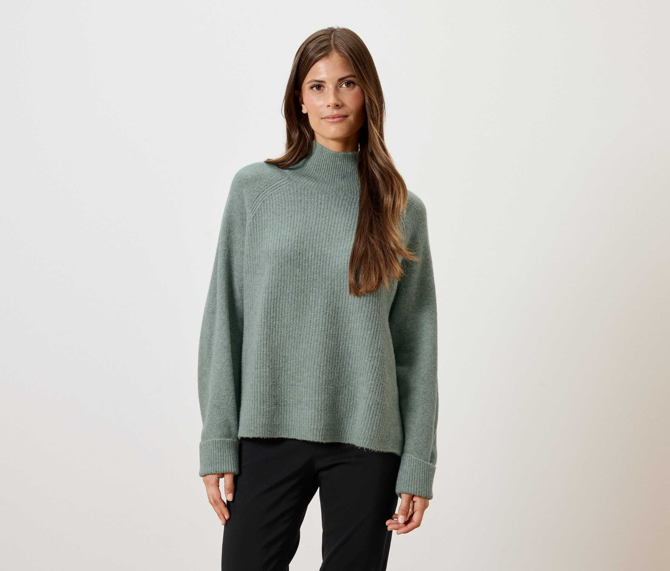 Femme portant un pull vert et un pantalon noir.