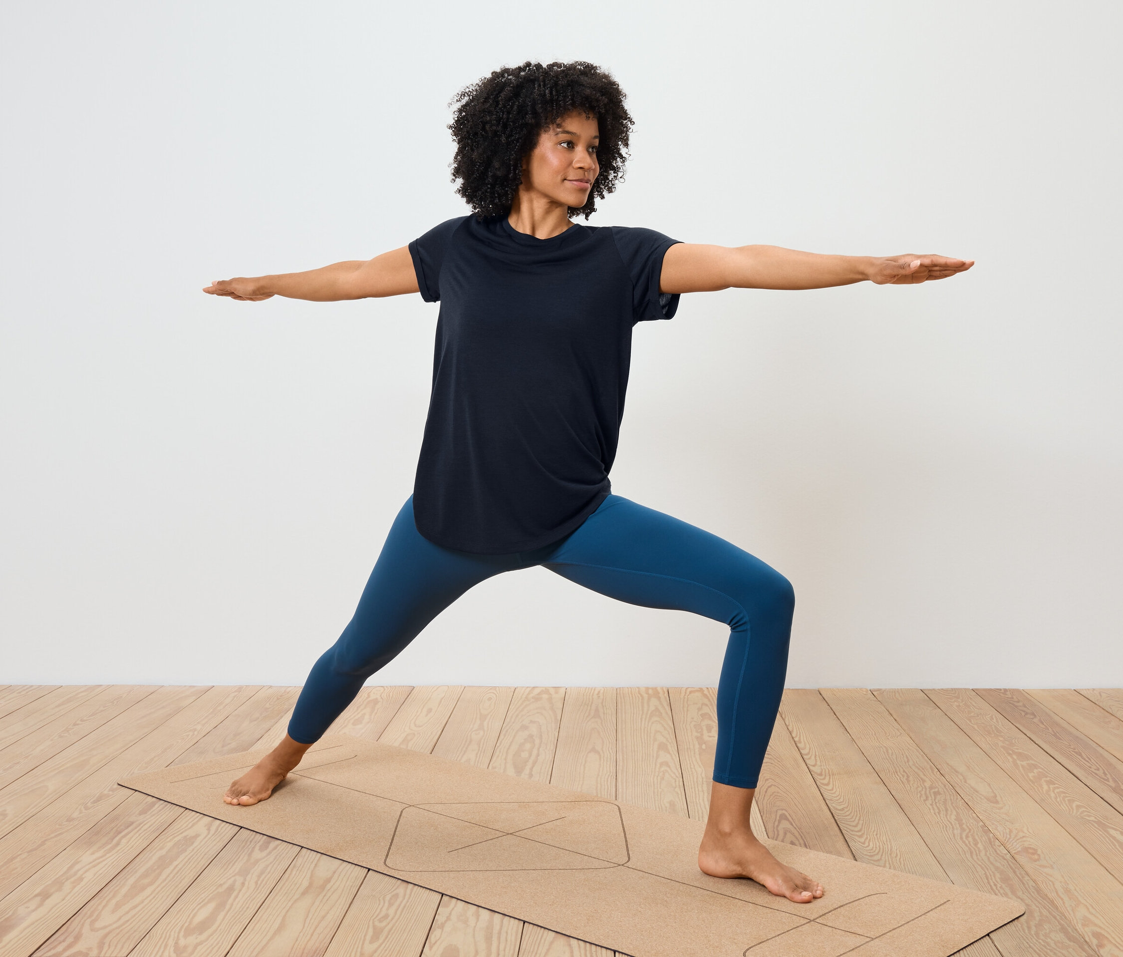 Femme en leggings bleus et t-shirt noir faisant du yoga sur un tapis.