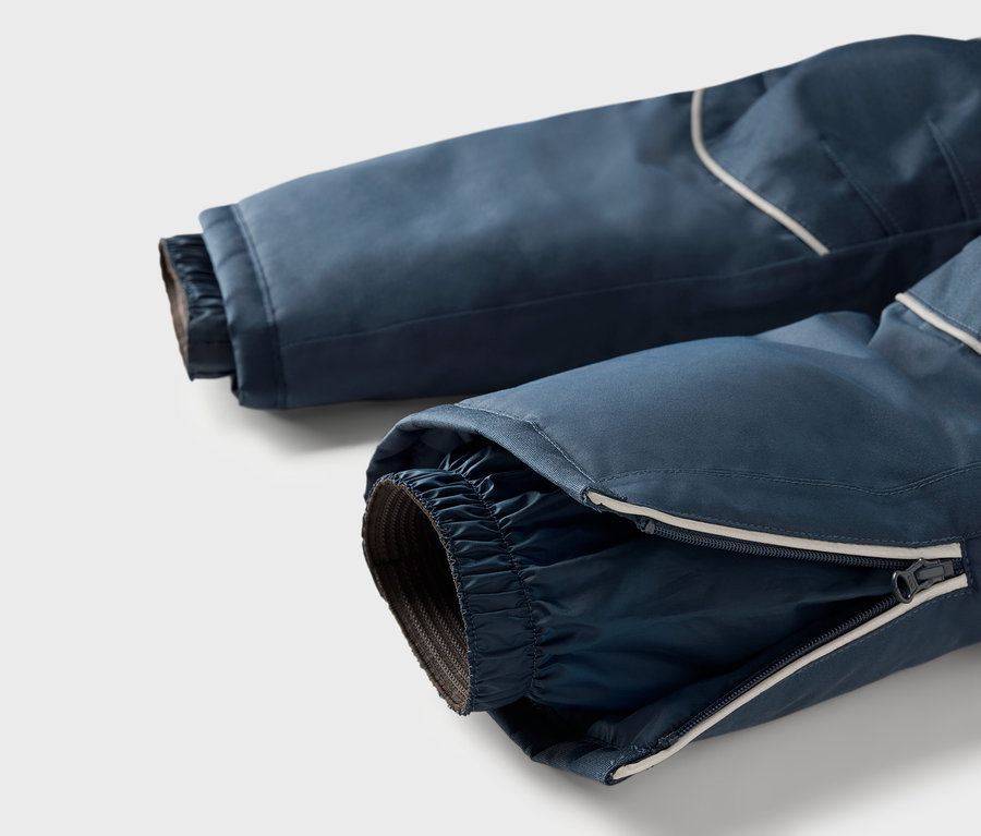 Détail d'un pantalon de ski bleu avec fermeture éclair sur la jambe et bande réfléchissante.
