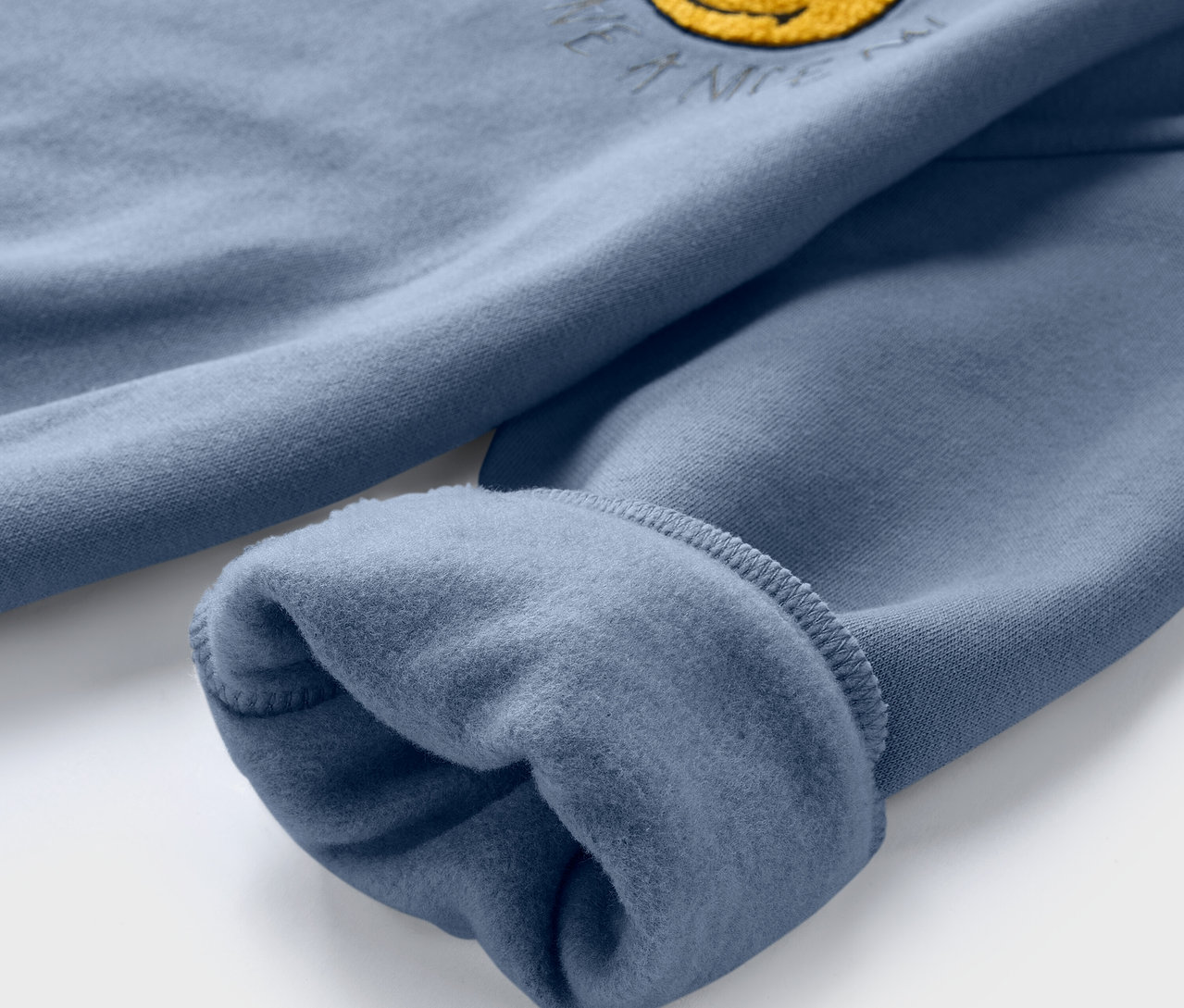 Gros plan sur un sweatshirt bleu pour enfant SMILEYWORLD® avec intérieur gratté et smiley jaune.