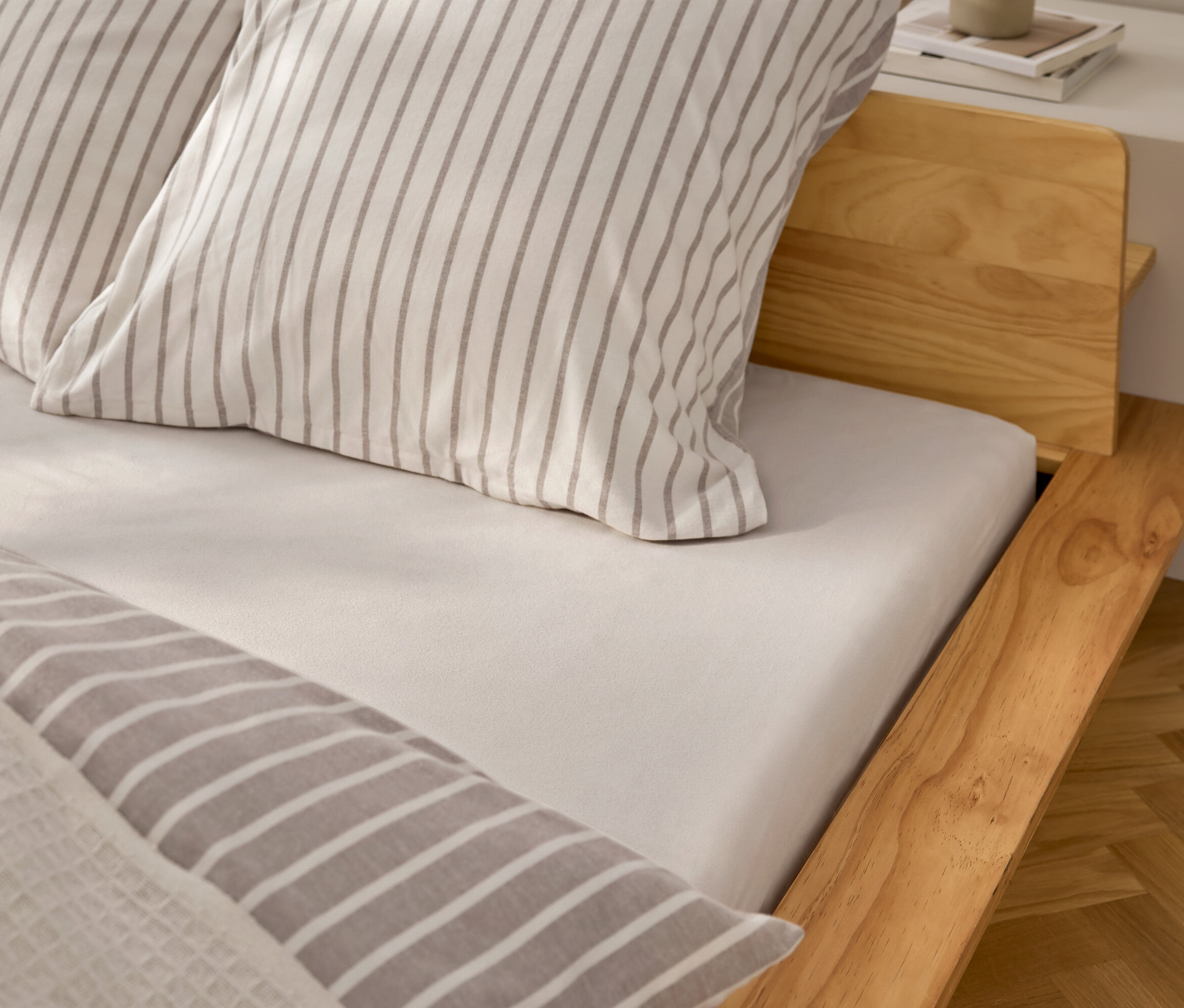 Vue détaillée d'un lit avec un drap-housse blanc et des oreillers à rayures grises.