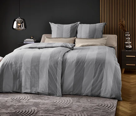 Chambre avec un lit avec des draps rayés gris, deux oreillers et une table de chevet.