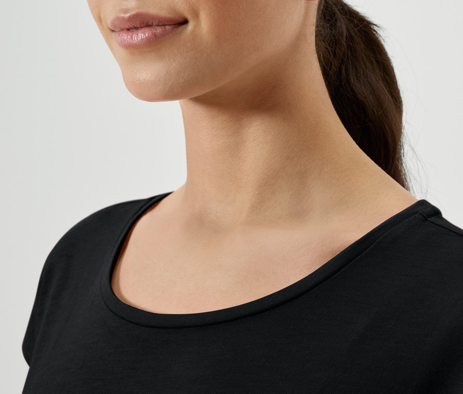 Gros plan sur une femme aux cheveux bruns attachés en queue de cheval, portant un t-shirt noir.