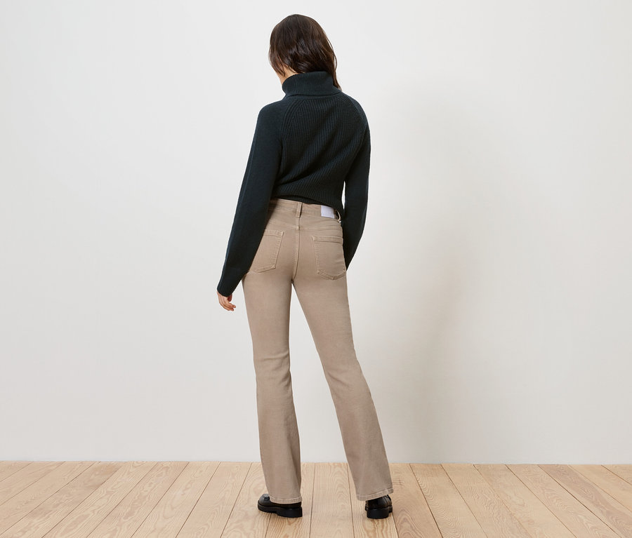 Vue de dos d'une femme portant un pull à col roulé foncé et un jean beige évasé.