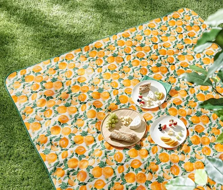 Nappe de pique-nique XL à motif d'oranges avec de la nourriture dessus sur l'herbe.