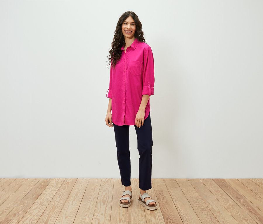 Une femme debout portant une blouse longue en lin rose vif.