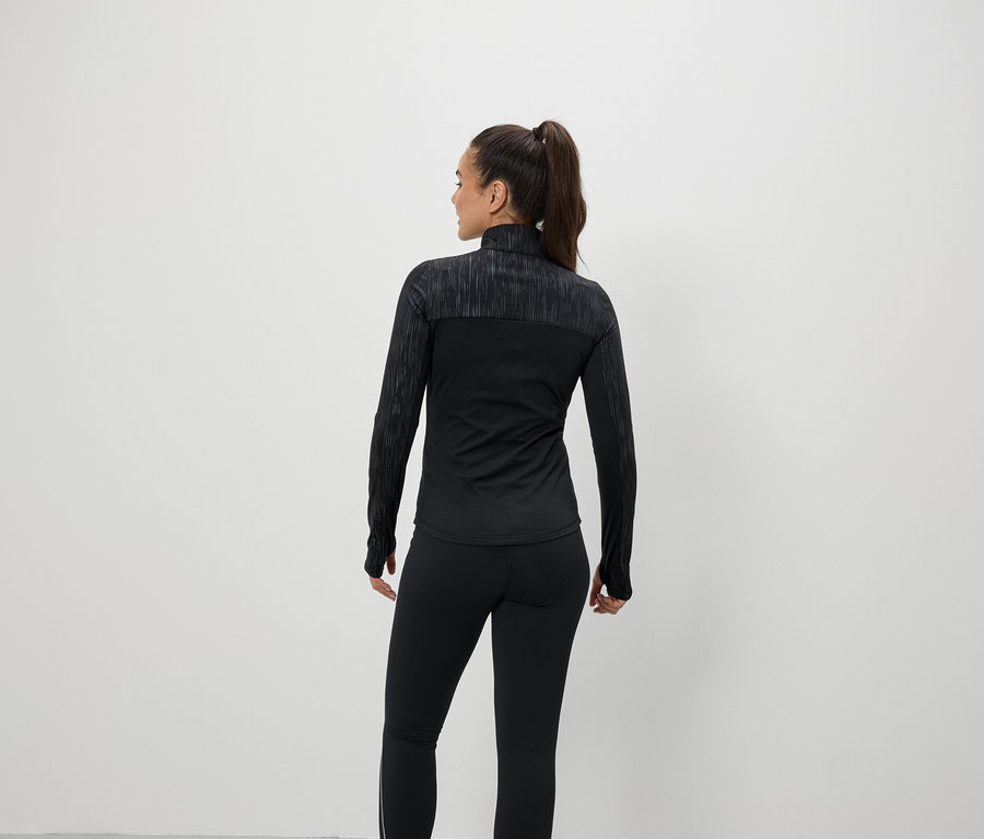 Une femme, dos à la caméra, porte des vêtements de sport noirs.