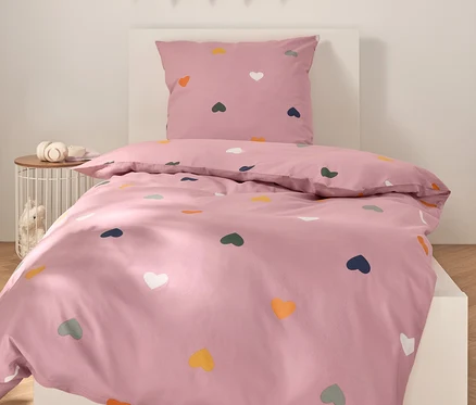 Linge de lit rose avec des cœurs colorés sur un lit blanc.