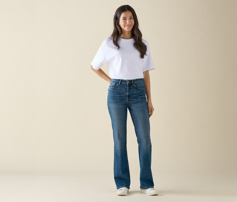 Une femme portant un t-shirt blanc et un jean bleu pose debout.