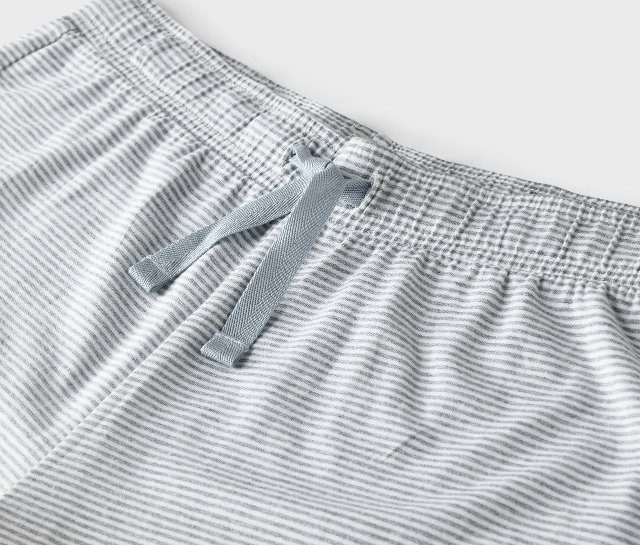 Détail d'un pantalon rayé gris et blanc avec un cordon de serrage bleu à la taille.