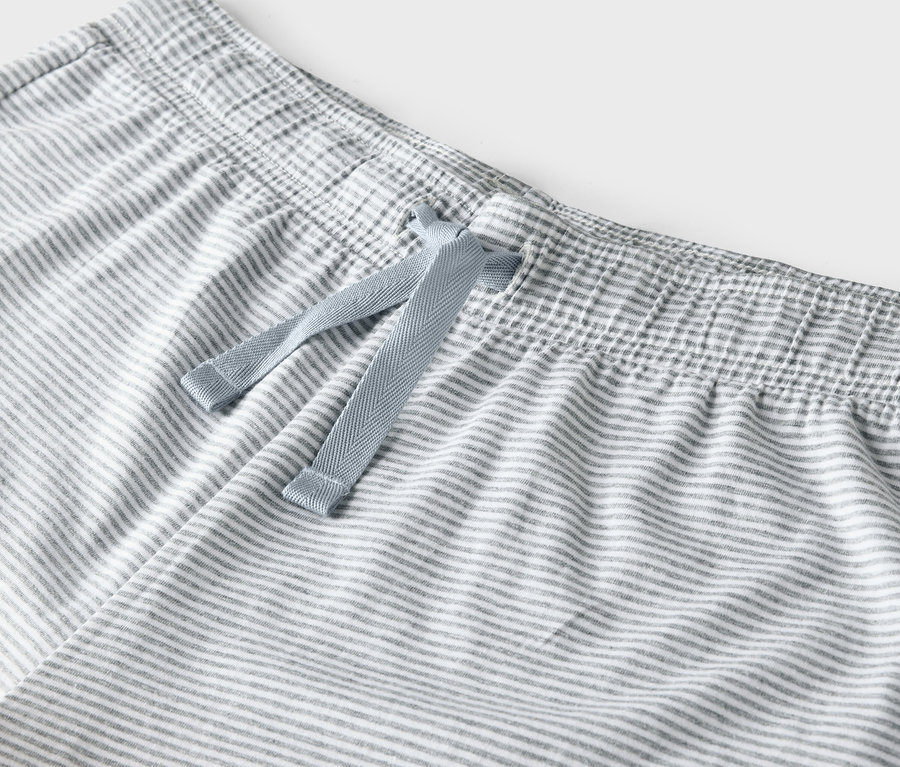 Détail d'un pantalon rayé gris et blanc avec un cordon de serrage bleu à la taille.
