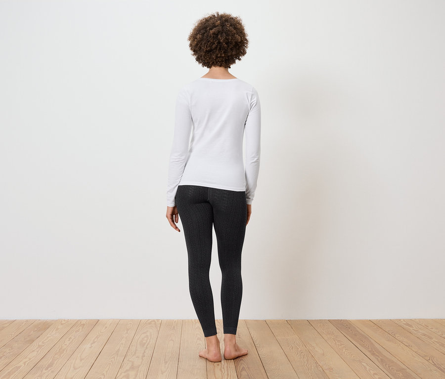 Une femme avec une coiffure afro est de dos, portant un t-shirt blanc à manches longues et un legging noir.