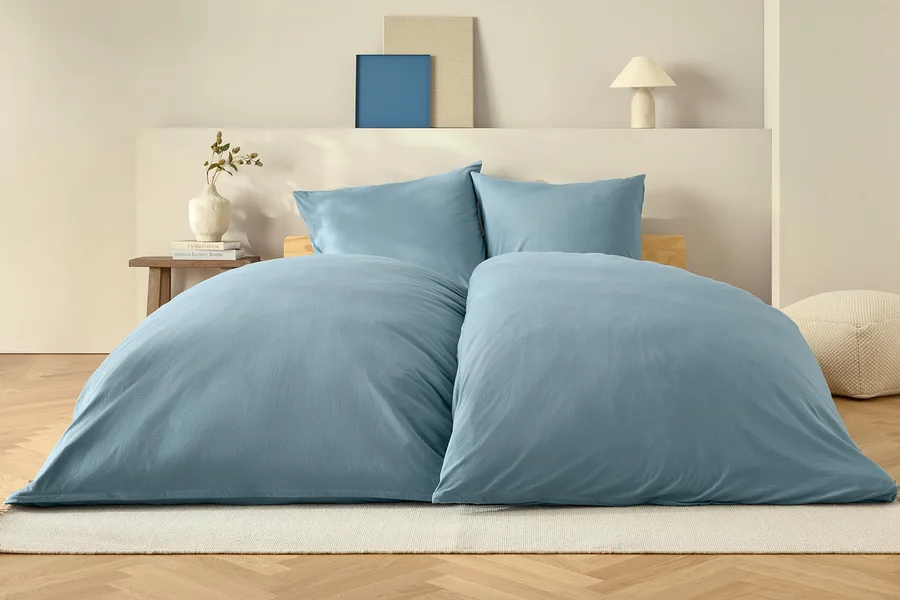 Couette bleue et deux oreillers sur un lit sur un tapis blanc.