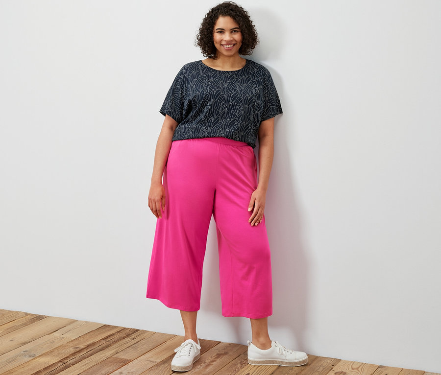 Une femme debout porte un chemisier bleu foncé à manches courtes et un pantalon jersey rose.