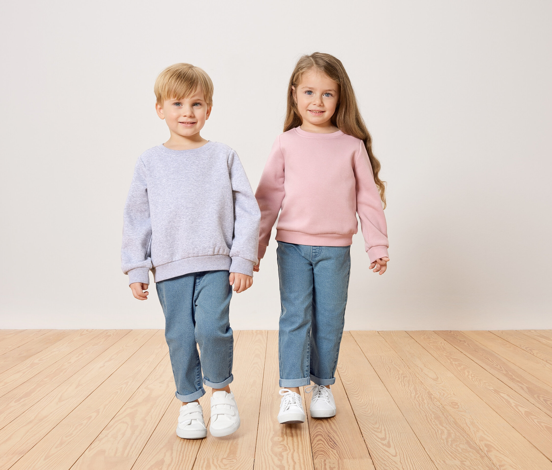 Un garçon en pull gris et une fille en pull rose se tiennent la main.