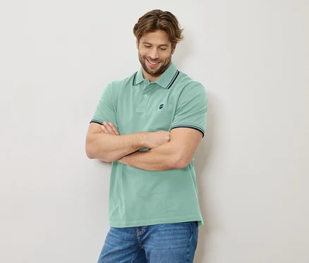 Homme aux bras croisés, portant un polo vert clair et un jean.