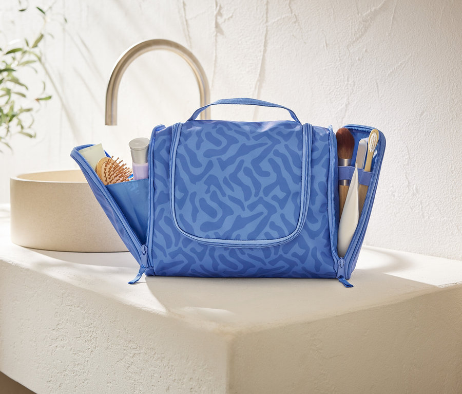 Une trousse de toilette bleue ouverte avec un motif abstrait est posée sur un comptoir blanc dans une salle de bain.