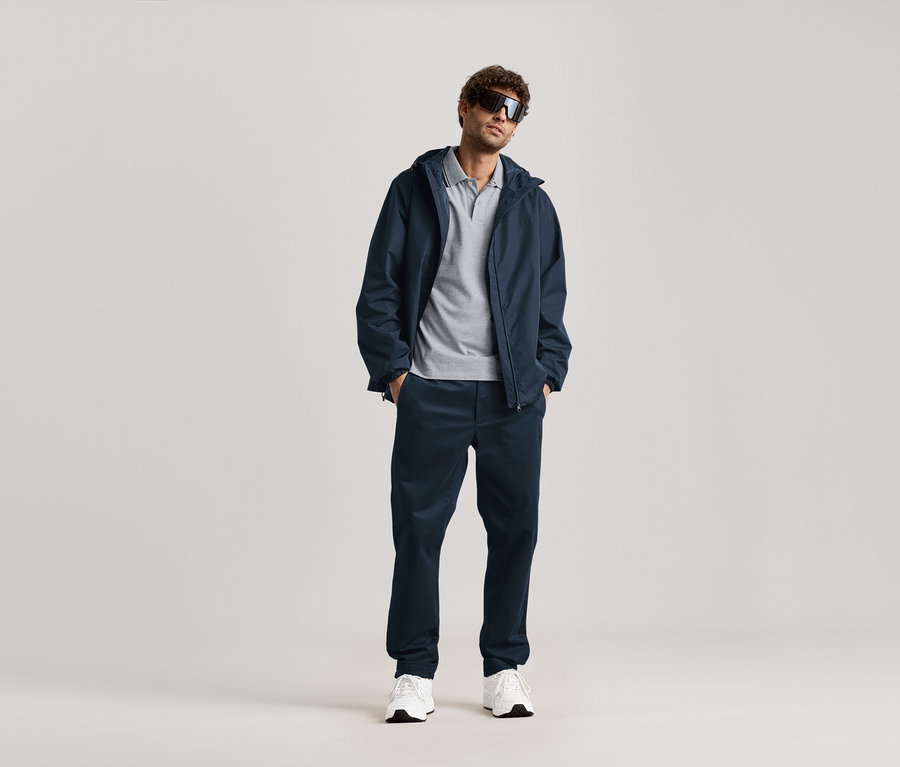 Un homme se tient debout avec des lunettes de soleil, une veste bleu marine et un chino bleu marine.
