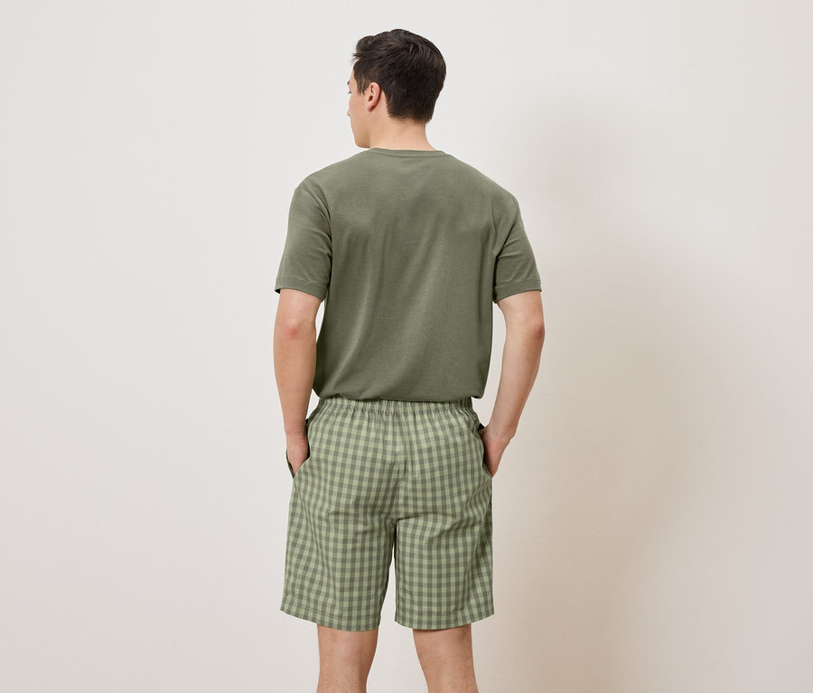 Un homme, dos à la caméra, porte un t-shirt vert et un short à carreaux verts.