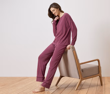 Femme en pyjama bordeaux appuyée sur une chaise.