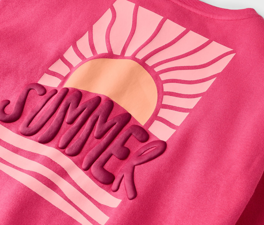 Sur un sweat-shirt rose figure un motif avec l'inscription "SUMMER" et un soleil.
