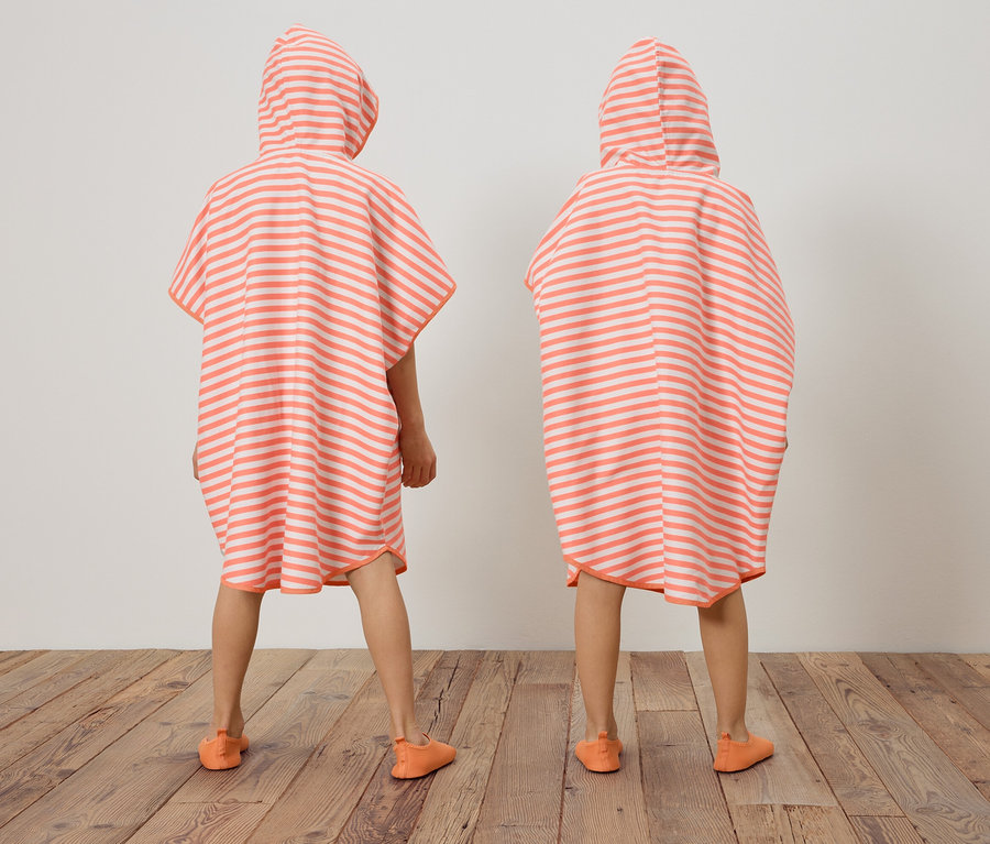 Deux enfants, de dos, portent des ponchos rayés corail et blanc à capuche et des chaussures assorties.