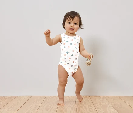 Un bébé se tient sur un plancher en bois et tient un jouet.