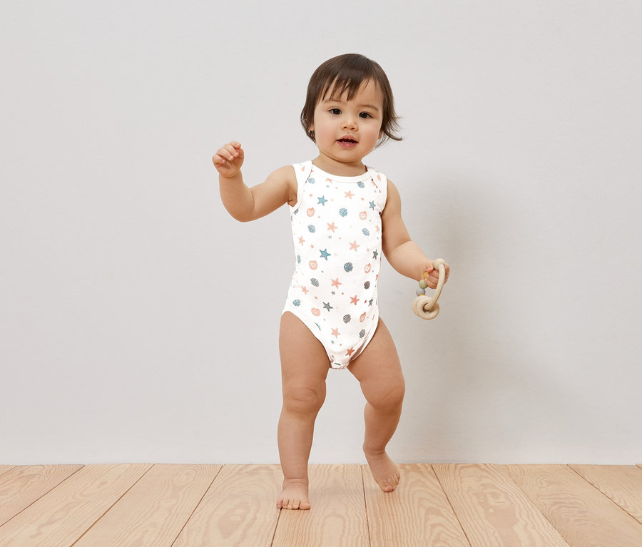 Un bébé se tient sur un plancher en bois et tient un jouet.