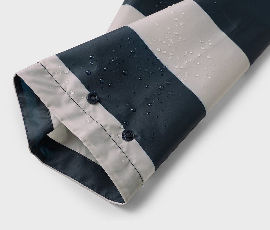 Manche d'un imperméable à rayures bleu et blanc avec des gouttes d'eau et deux boutons-pression.