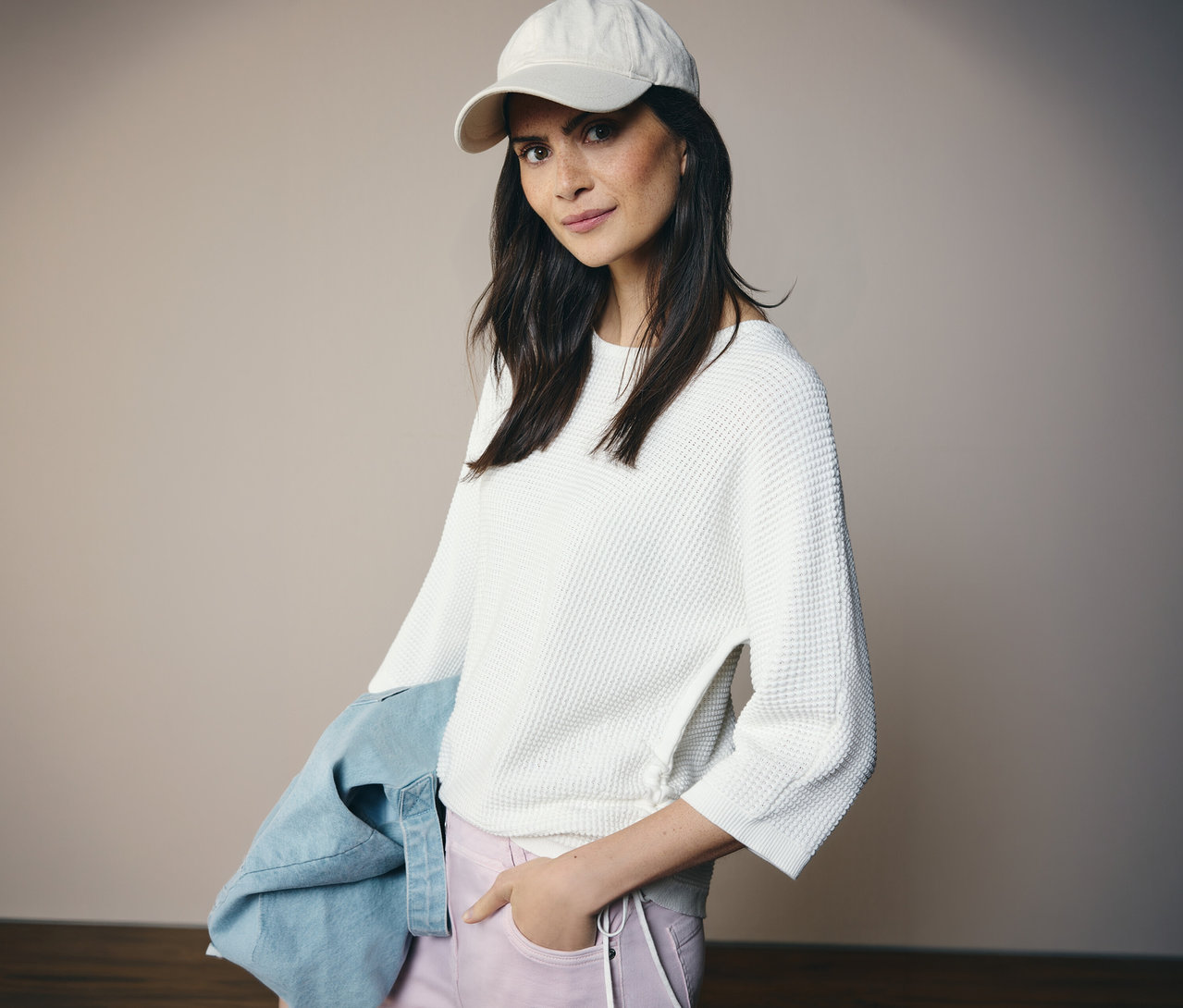 Femme portant une casquette blanche et un pull en maille fine CECIL, une veste en jean sur le bras, la main dans la poche.