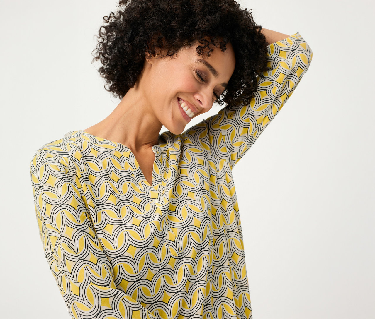 Femme souriante portant un chemisier Olsen 3/4 jaune à motifs.