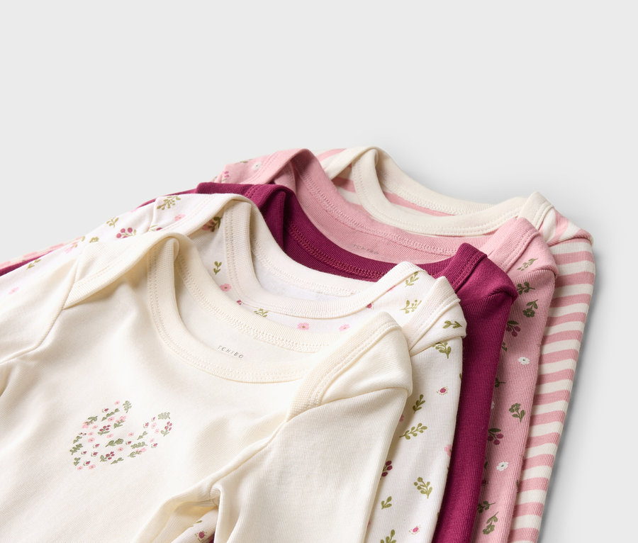 Pile de cinq bodies pour bébés en blanc, rose et violet avec différents motifs floraux et rayures.