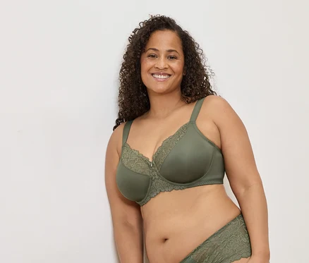 Femme souriante aux cheveux bouclés portant un soutien-gorge vert olive avec de la dentelle et des sous-vêtements assortis.