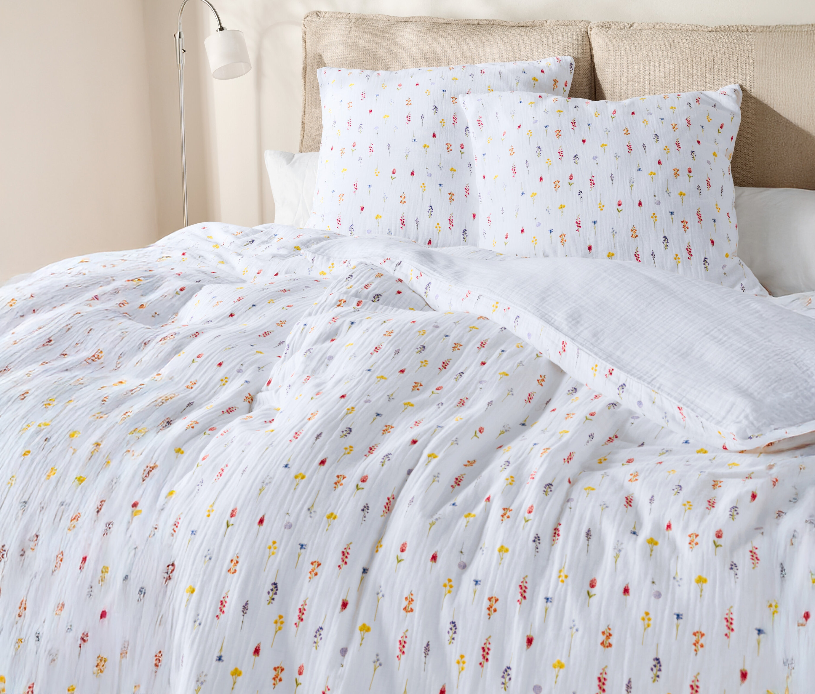 Gros plan d'un lit avec des draps blancs à motifs floraux et des oreillers.