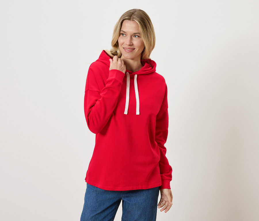 Une femme porte un sweat à capuche rouge et un jean.