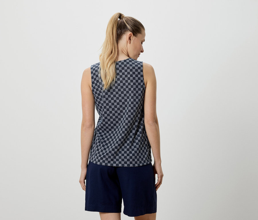 Vue arrière d'une femme blonde portant un haut bleu sans manches à motif géométrique blanc et un short bleu marine.