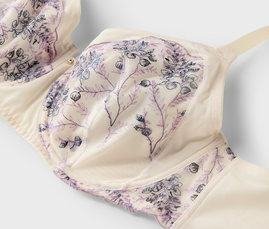 Gros plan d'un soutien-gorge couleur crème avec de délicates broderies florales violettes sur fond blanc.