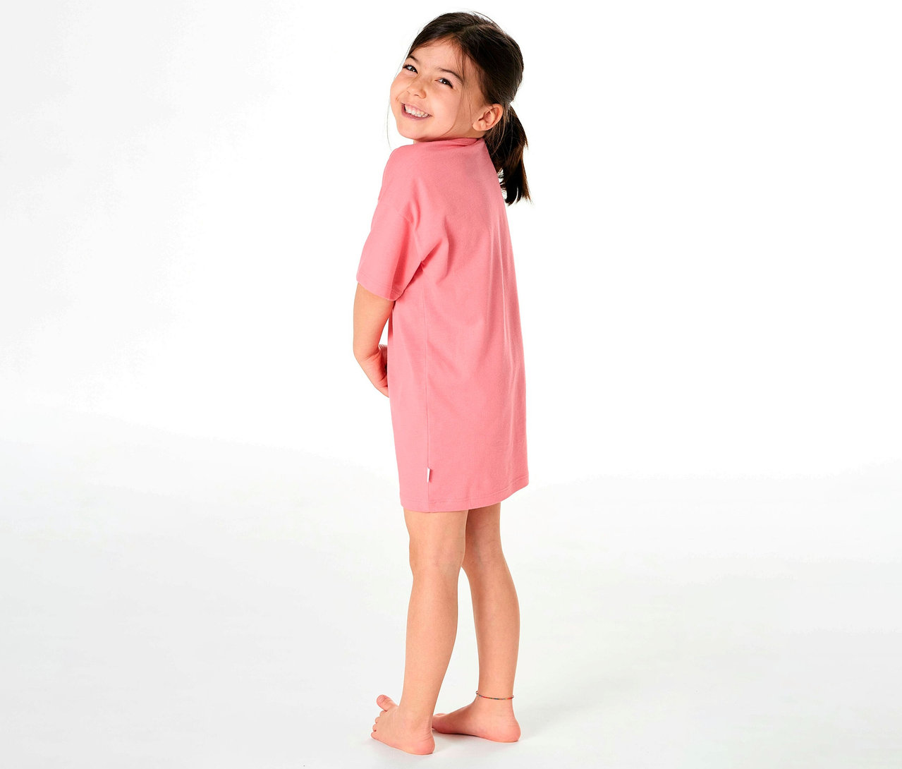 Fillette regardant par-dessus son épaule et portant une chemise de nuit pour enfant SCHIESSER rose.