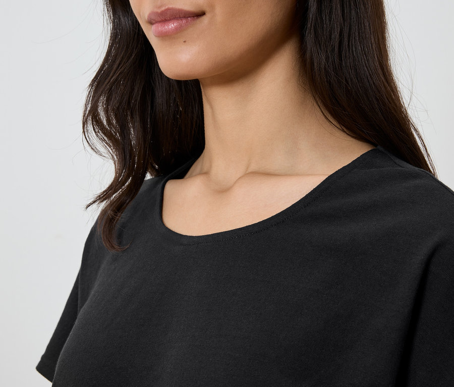 Gros plan d'une femme aux cheveux ondulés foncés, portant un t-shirt noir.