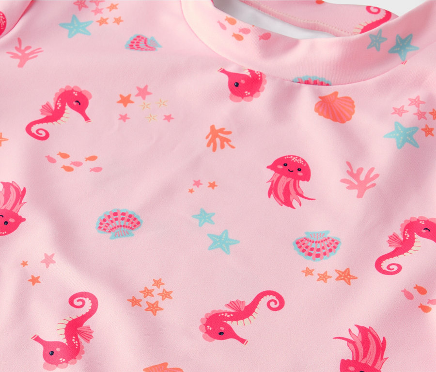 Gros plan d'un tissu rose avec des motifs d'hippocampes, de méduses et de coquillages.