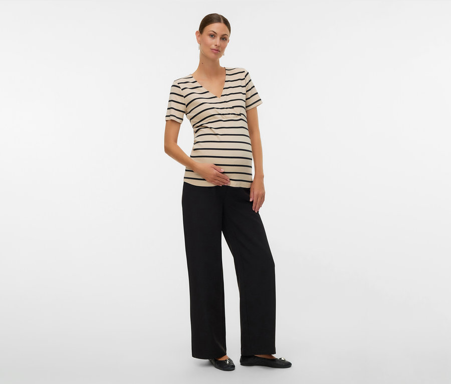 Femme portant un t-shirt de grossesse MAMALICIOUS « MLLANE TESS » rayé noir, un pantalon noir et des ballerines, main sur le ventre.