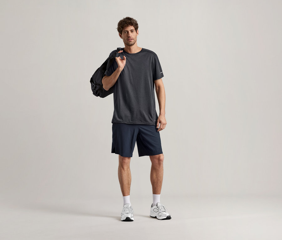 Homme portant un t-shirt de sport anthracite avec un sac de sport sur l'épaule.