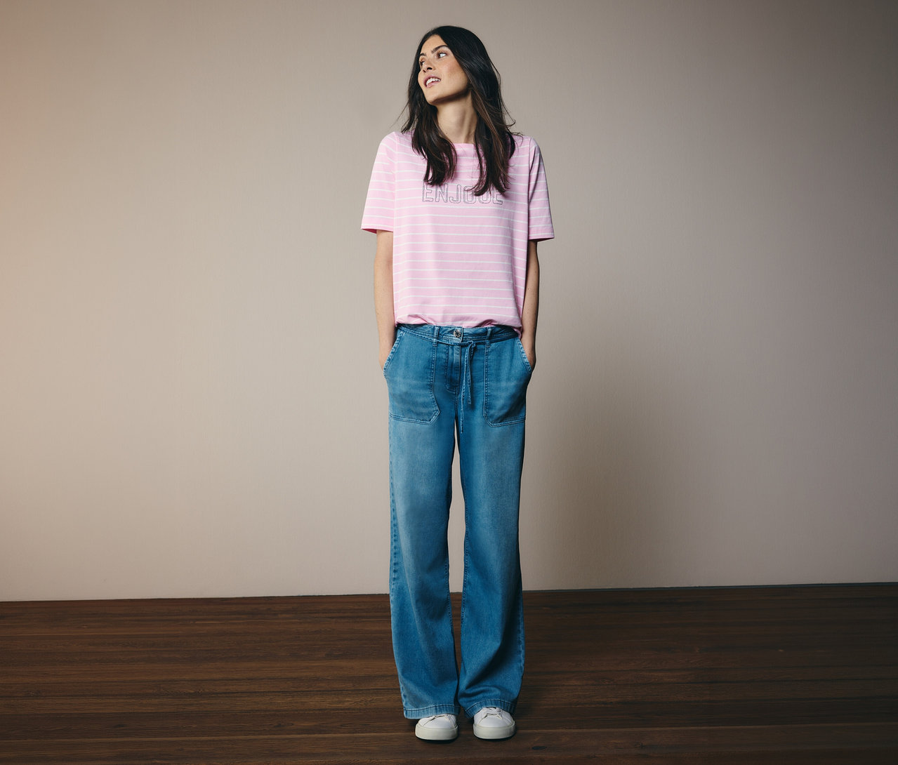 Femme portant un t-shirt rose rayé et un jean CECIL « Neele » debout devant un mur.