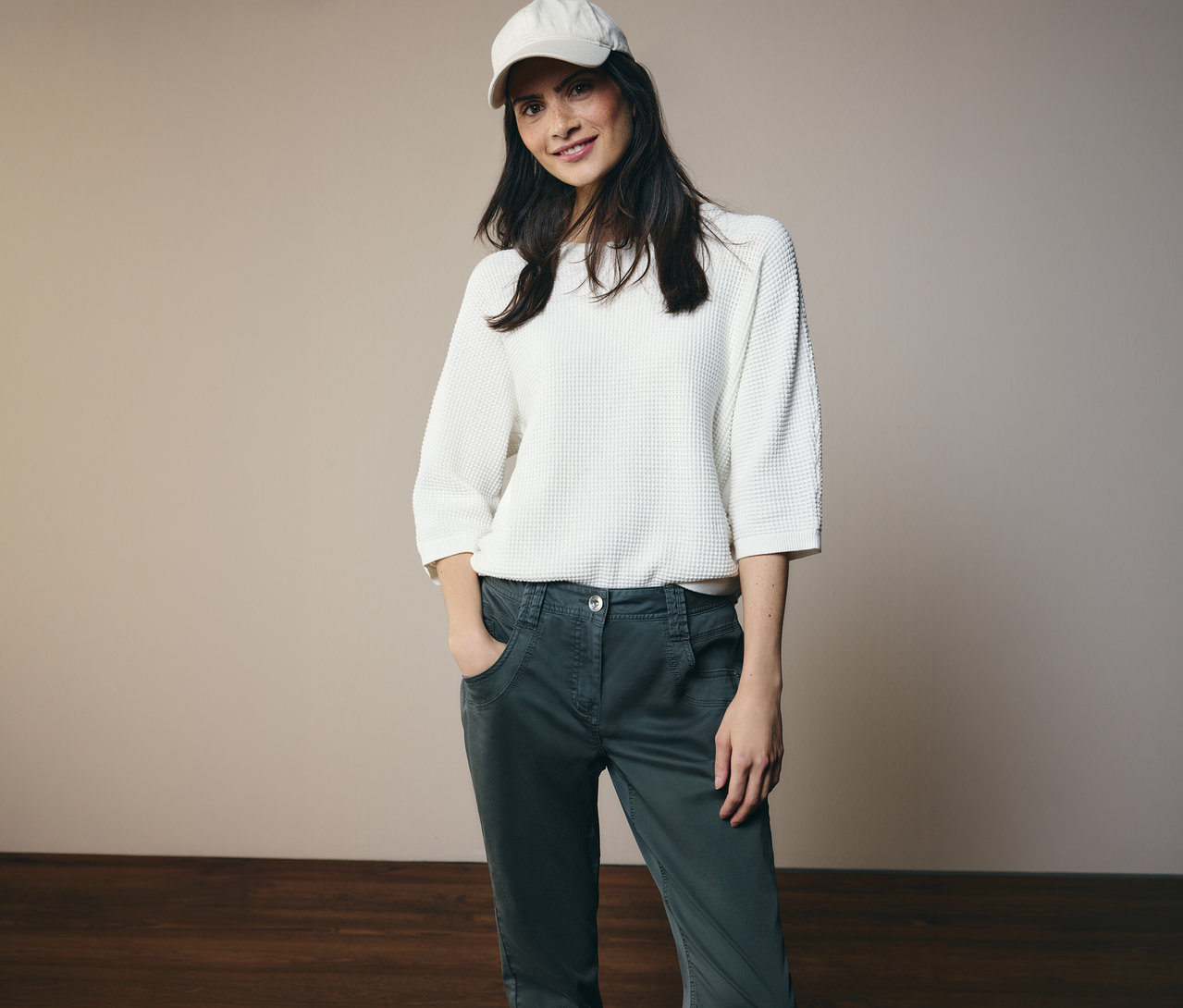 Une femme portant un haut blanc et une casquette pose en pantalon CECIL « Scarlett » avec les mains dans les poches.